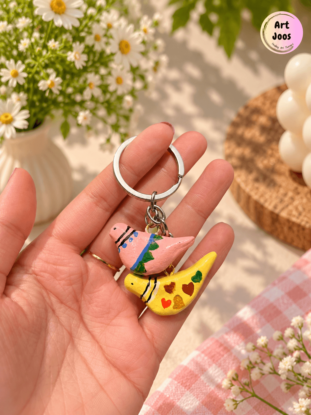 Handmade clay keychain featuring two colorful bird charms, one pink with blue and green details and one yellow decorated with colorful hearts, attached to a silver-tone metal keyring.
