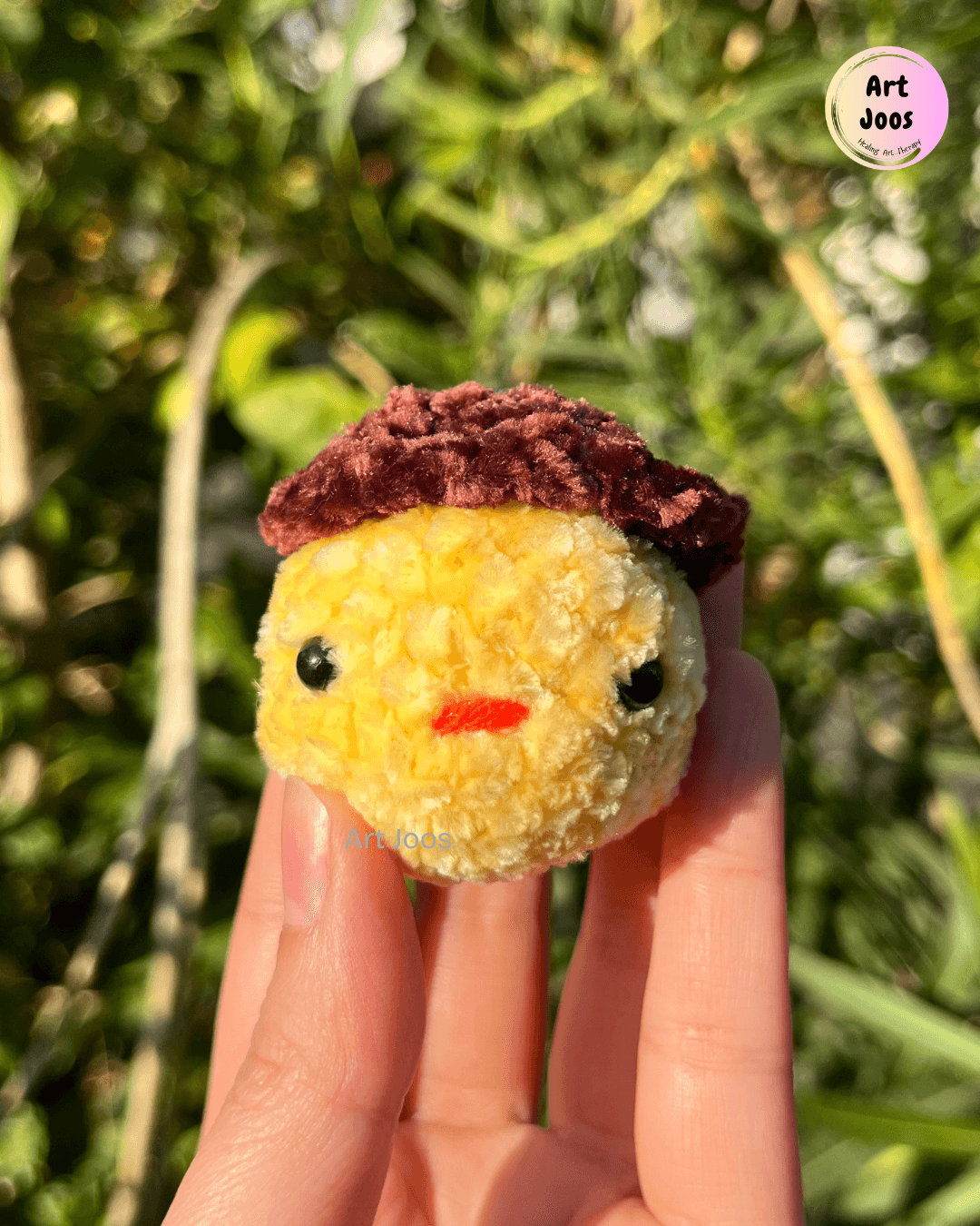 Handmade yellow plush crochet keychain with a chocolate-brown cap, black eyes, a tiny red embroidered mouth, and a silver-tone metal chain.