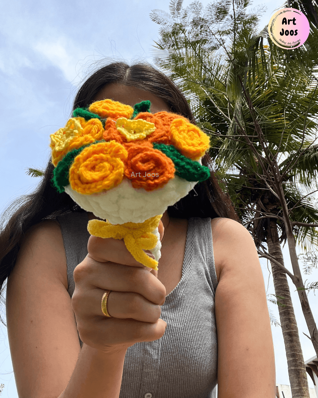 Handmade crochet mini bouquet featuring bright orange and yellow roses, dark green leaves, and a soft white base with a yellow accent, held in a hand.