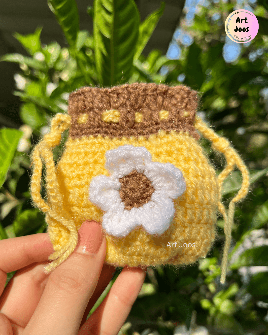 Handmade honey-yellow crochet drawstring pouch shaped like a jar, featuring a textured brown lid, yellow accents, and a white daisy with a brown center.