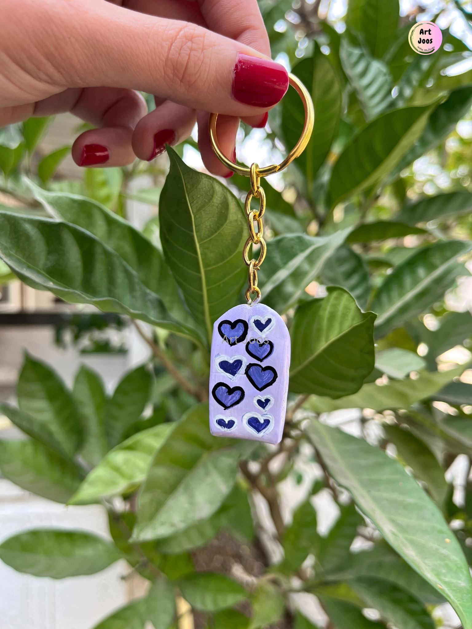 Handmade lavender clay keychain decorated with navy-blue and black hearts, attached to a gold-tone metal chain and circular keyring.