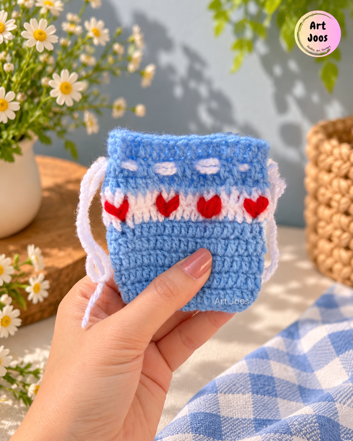 Pastel blue handmade crochet drawstring pouch featuring a white band with four red hearts and white decorative accents.